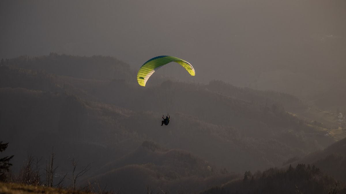 Paraglider with a yellow-green wing against dark misty hills