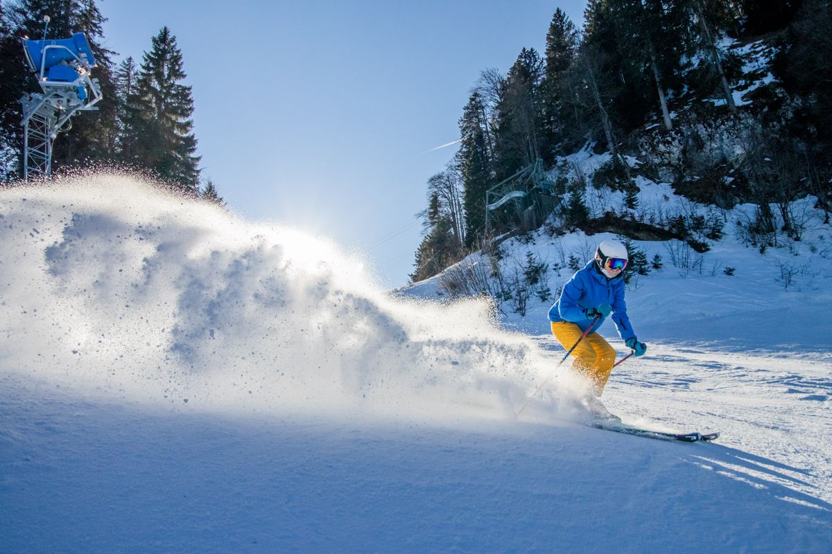 Skier in a blue jacket throwing up a wall of powder