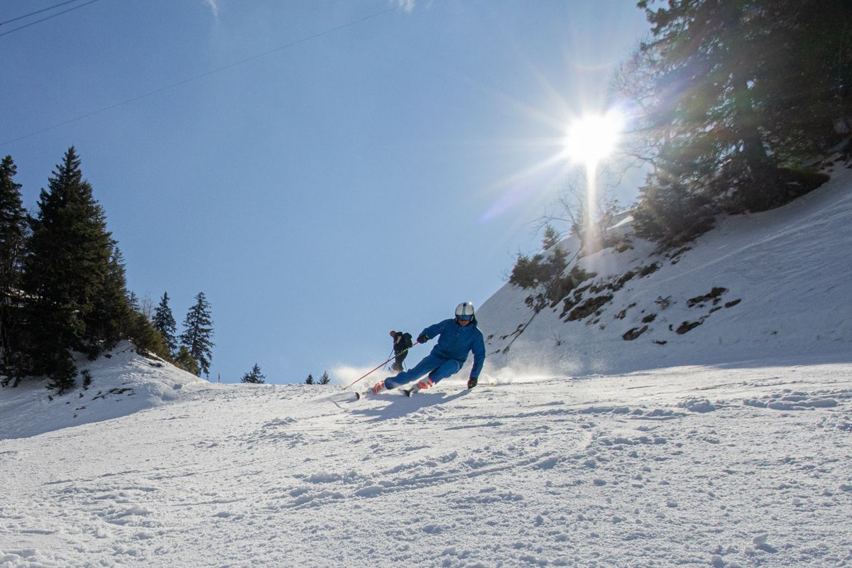 Skier carving past a second skier under a bright sun