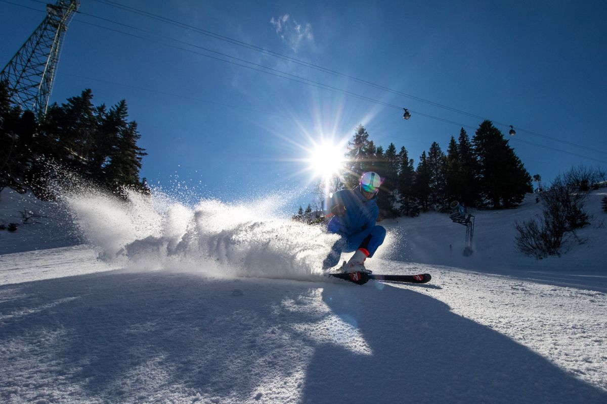 Skier spraying snow under a low sun and a gondola line