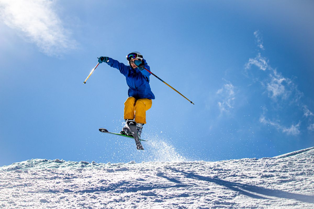 Skier in yellow trousers jumping against a blue sky
