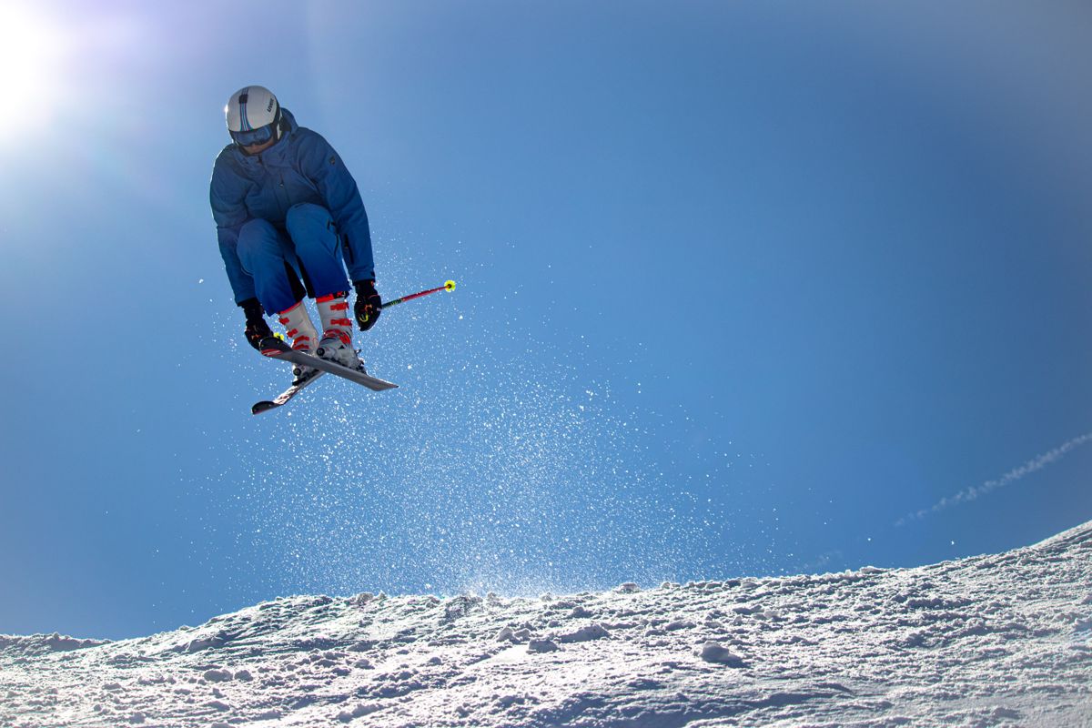 Skier crossing skis mid-jump against a blue sky