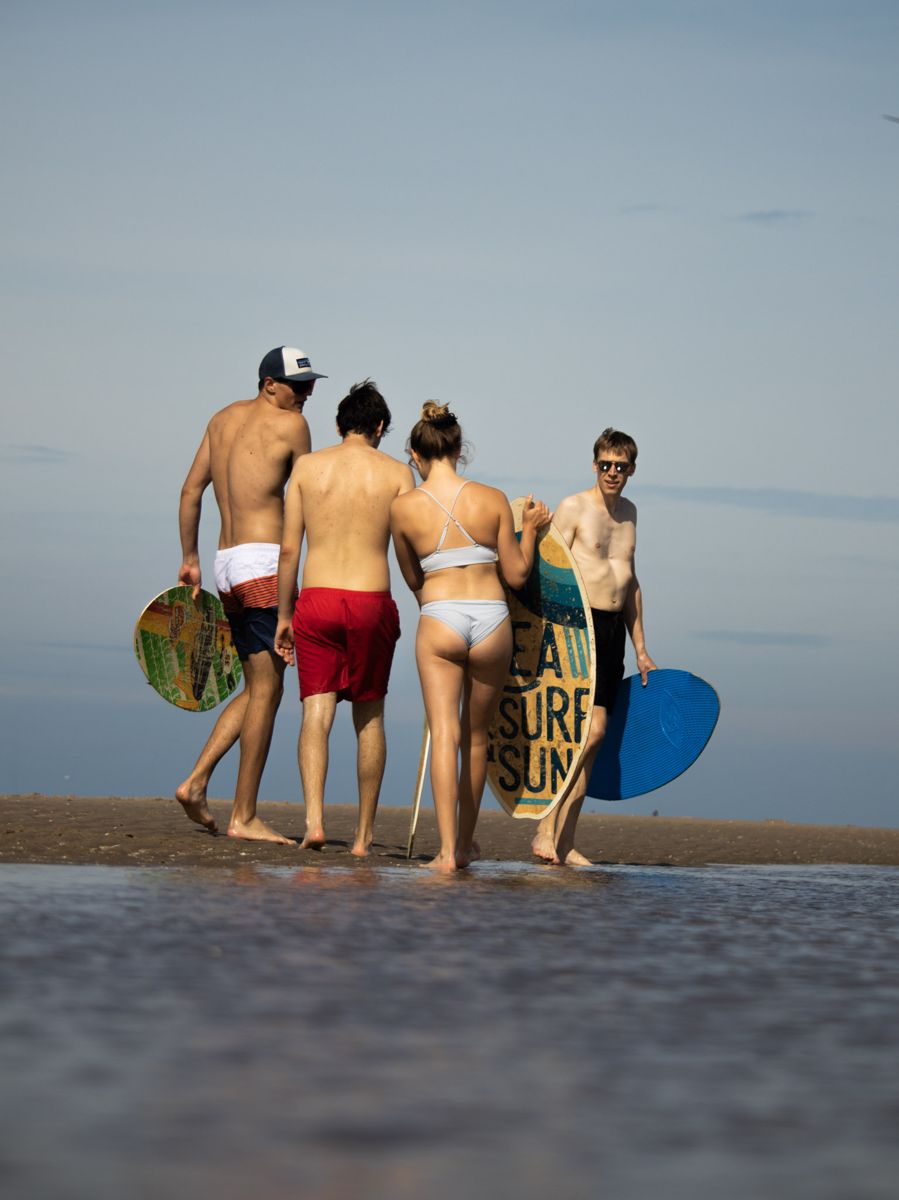 Four friends carrying skimboards across the sand