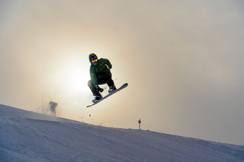 Snowboarder mid-jump against a hazy sun