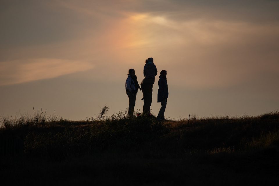 Three people silhouetted on a dune at sunset